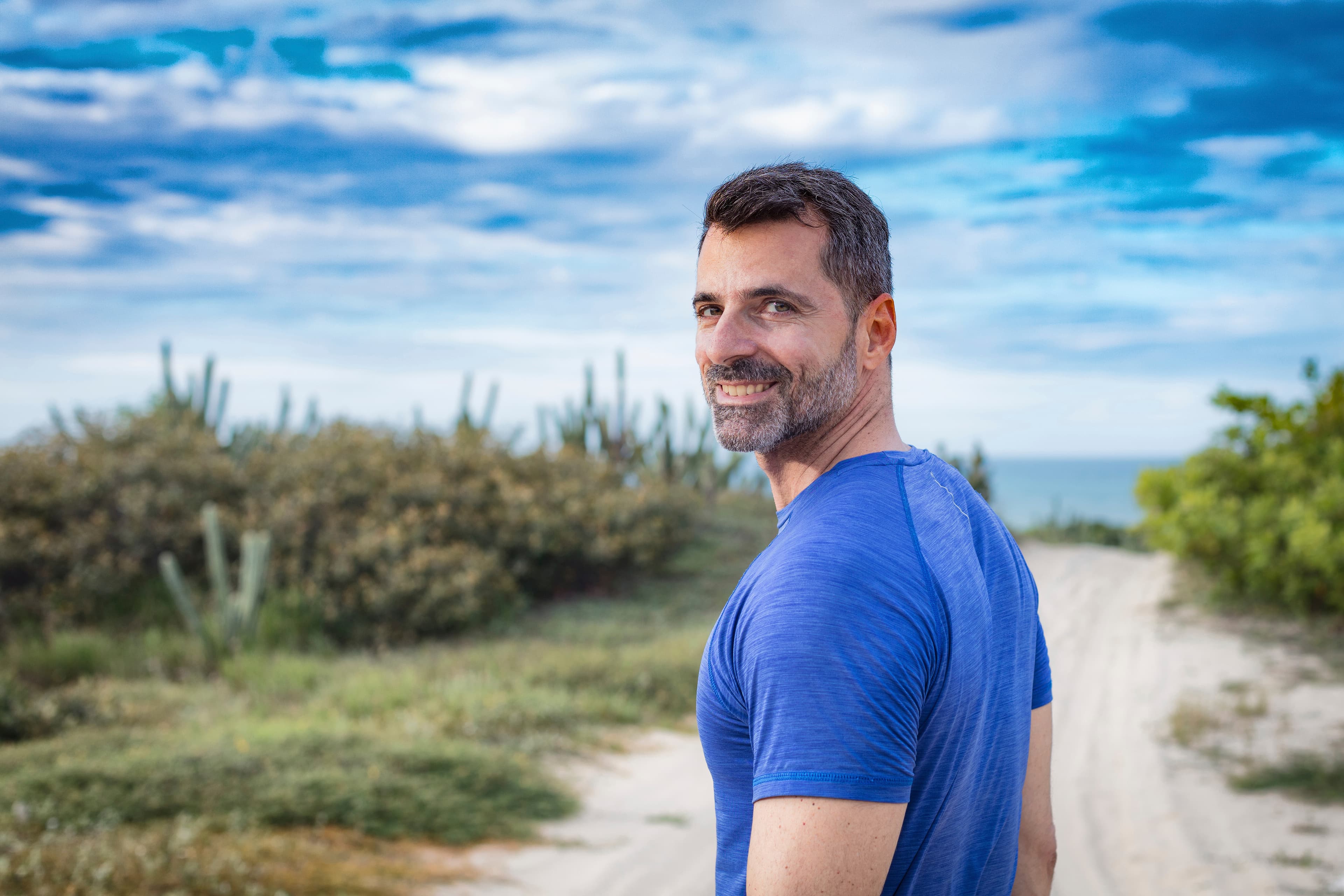 Middle-aged man walking on a coastal gravel path, looking back with a smile